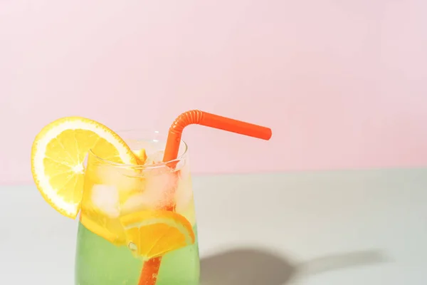 stock image Glass cup with straw with citrus drink with ice against pink background.