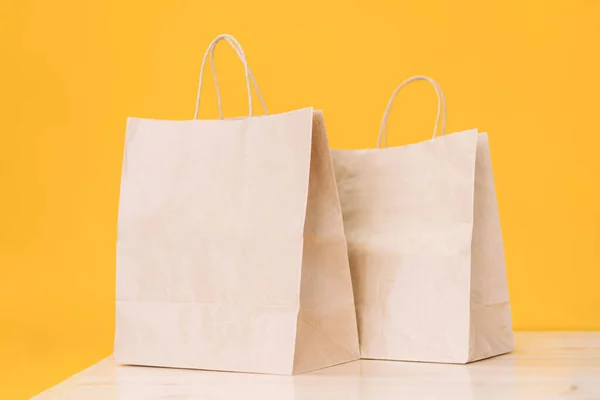 stock image Craft paper bags on wooden table against yellow background.