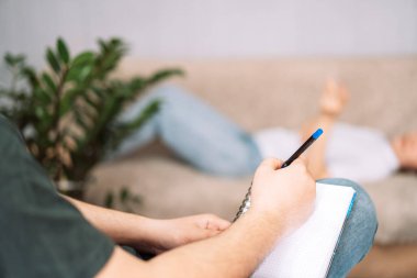 Kadın psikoloğa söyler, psikolog da deftere yazar..