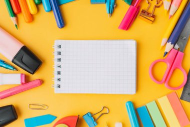 Sarı arka planda okul malzemelerinin etrafında boş kağıtlar olan not defteri..