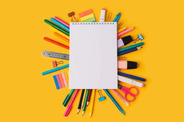 Sarı arka planda okul malzemelerinin üzerinde boş kağıtlar olan not defteri..