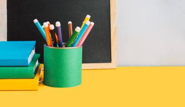 Sarı arka planda kitap ve tebeşirle okul malzemeleri..