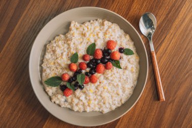 Ahududulu yulaf ezmesi ve beyaz bir fincanda kuşüzümü ve kaşık..