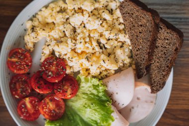 Dilimlenmiş sebze, çırpılmış yumurta ve ahşap masada beyaz tabakta jambon..