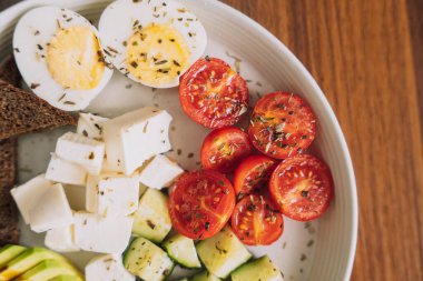 Peynirli ve yumurtalı sebze salatası ve beyaz tabakta çavdar ekmeği.