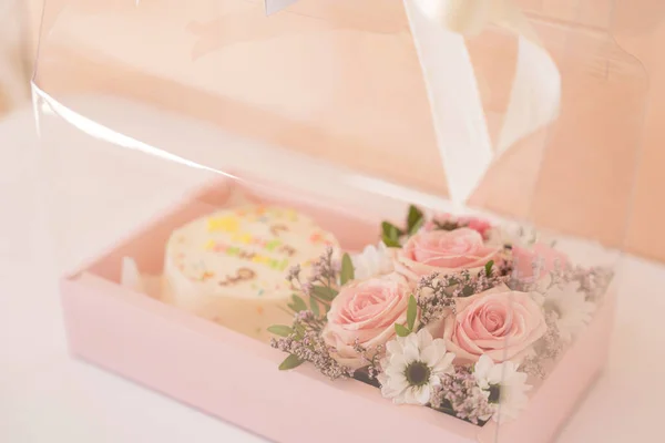 Gift for a teacher in transparent box with bow. Round white cake with blooming roses.