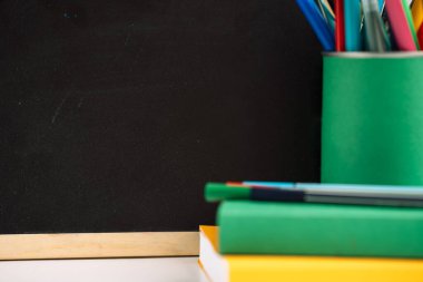 Tahtanın önünde renkli kitaplarla okul malzemeleri..