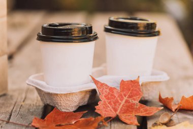 Kırmızı akçaağaç yapraklı sıcak bir içecek içeren beyaz bardaklar..