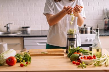 Mutfaktaki kadın taze sebzelerin olduğu ahşap bir masada kereviz karıştırıcısına atıyor..