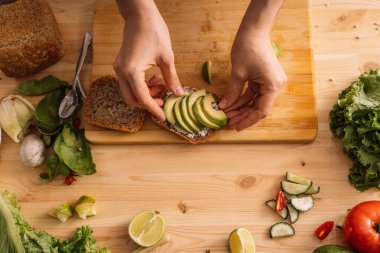 Bayan taze sebzelerin arasında, tahtadan bir masada vejetaryen sandviç hazırlıyor..