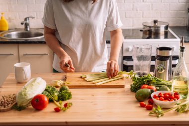 Mutfaktaki kadın taze sebzelerin olduğu ahşap bir masada kereviz doğruyor..