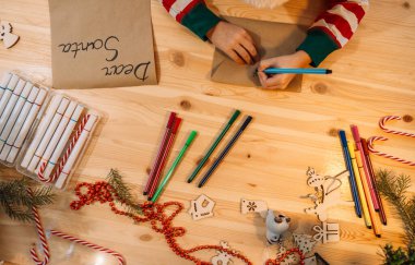 Bir çocuk Noel Baba 'ya mektup yazıyor. Kalemlerin ve Noel süslerinin arasındaki tahta masaya..