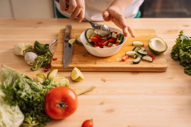 Bayan, ahşap bir masada beyaz bir tabakta kaşıkla vejetaryen salatası karıştırıyor..