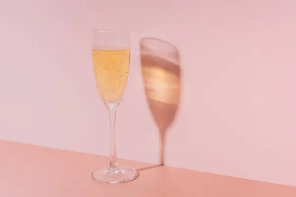 Glass of champagne with bubbles against pink background.
