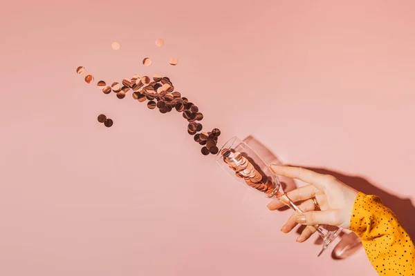 Ladys hand holding a glass from which large round sparkles fly out against a pink background.