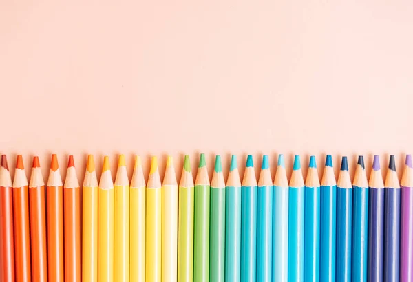 Colored rainbow pencils lie in a row on a beige background.