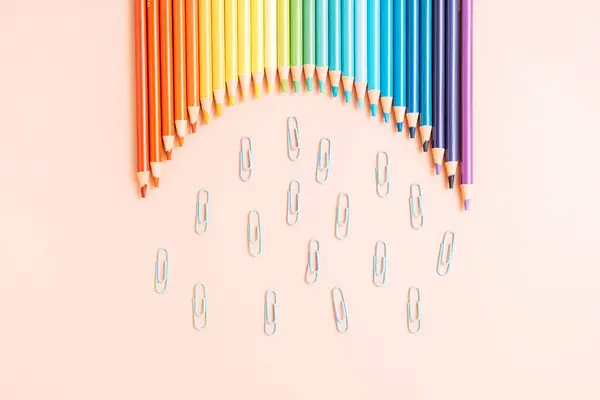 Colored rainbow pencils lie in a row with paper clips on a beige background.