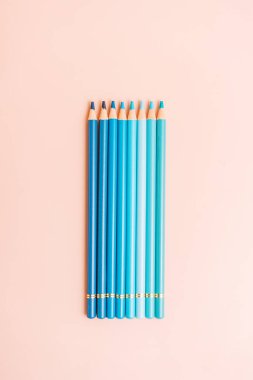 Blue pencils lie in a row on a beige background.