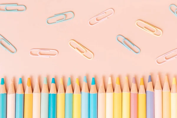 Colored pencils and paper clips on a beige background.