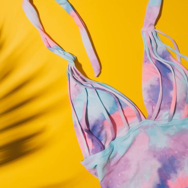 Sarı arkaplanda çok renkli mayo ve palmiye yaprağının gölgesi..