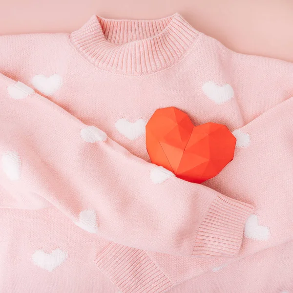 Pink sweater with white hearts hugs red origami heart shape.