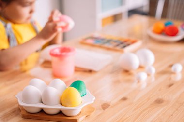 Küçük kız Paskalya için büyük tahta bir masada yumurta boyuyor..