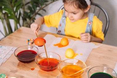 Küçük kız Paskalya için cam tabaklara yumurta boyuyor..