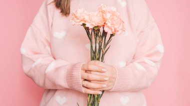 Bir buket karanfil kadın ellerinde pembe bir arka planda.