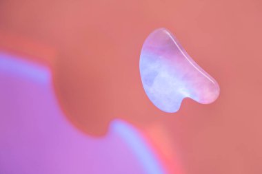 Turuncu arka planda sert mavi ışık altında Guasha yüz masajı. Yüksek kalite fotoğraf