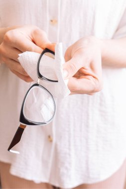 Bayan gözlüklerinin lenslerini ıslak mendille temizliyor. Dikey fotoğraf