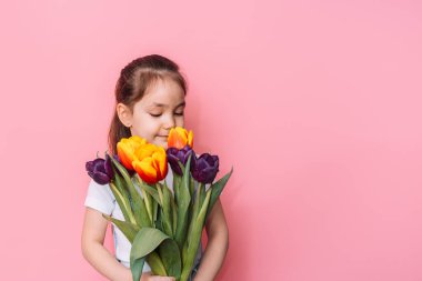 Çocuk pembe arka planda bir buket lale tutuyor..