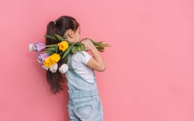 Küçük kız omuzunda pembe arka planda bir buket lale taşıyor..