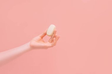 Pembe arka planda bir kalıp sabunu tutan bir kadın..