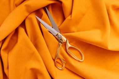 Turuncu kumaşın üzerinde duran makasın yakın çekimi.