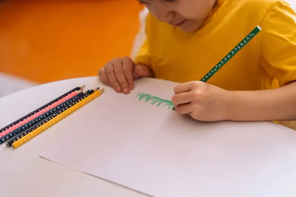 子供は紙のシートに緑の鉛筆でテーブルに描画する — ストック写真