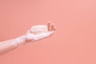 Kadın sabunlu eller pembe arka planda bir sabun parçası tutuyor..