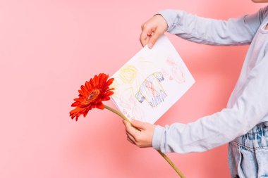 Babalar Günü tatili için elinde bir kartpostal ve çiçek tutan küçük bir kız pembe bir arka planda.