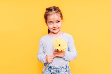 Anneler Günü 'nde elinde çiçek tutan çocuk sarı arka planda.
