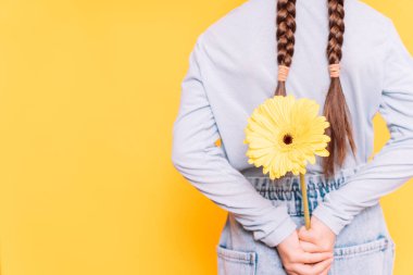 Sarı arka planda sarı çiçeği tutan çocuk.