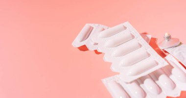 Paketlemedeki rektal mumlar ve pembe arka plandaki boş bir tüpte merhem..