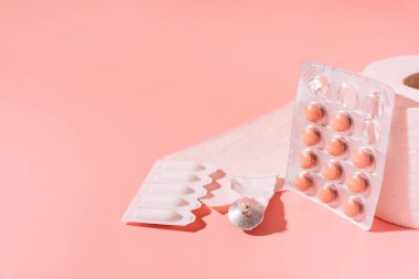 Tabletler, rektal mumlar ve merhemler pakette ve pembe arka planda tuvalet kağıdında.