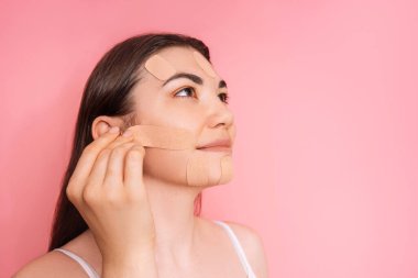 Yanağına pembe arkaplan bandı yapıştıran bir kadın..