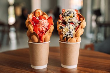 Dondurma bardaklarındaki köpüklü waffle 'lar ve ahşap masada çilekler..