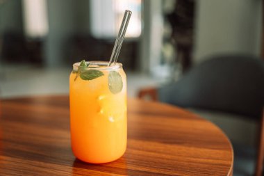 Cam bardakta buzlu portakal suyu ve ahşap masada saman..