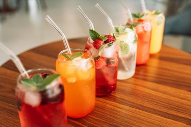 Böğürtlenli meyve içecekleri, cam bardaklarda buz ve ahşap bir masada pipetler..