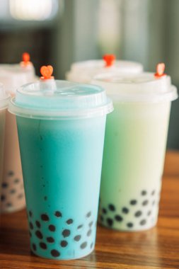 Plastik bardakta farklı aromalı baloncuk çayı ve ahşap bir masanın kapağı..