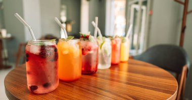 Böğürtlenli meyve içecekleri, cam bardaklarda buz ve ahşap bir masada pipetler..