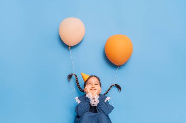 Helyum balonları, doğum gününü kutlayan küçük bir kızın örgülerine bağlıdır..