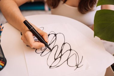 Lady draws with a black felt-tip pen on a white sheet. clipart