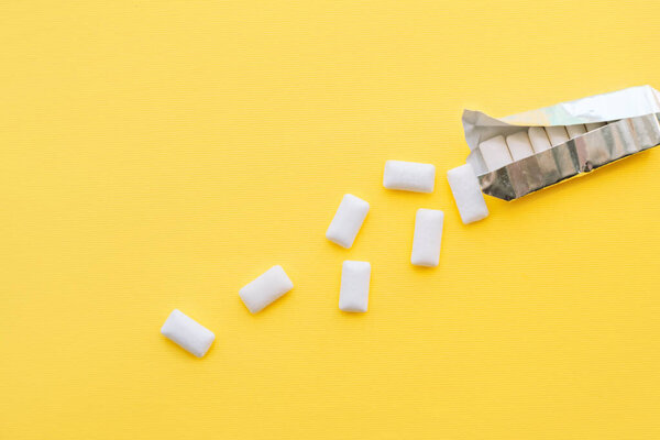 White chewing gum pads spilled out of a foil package on a yellow background.